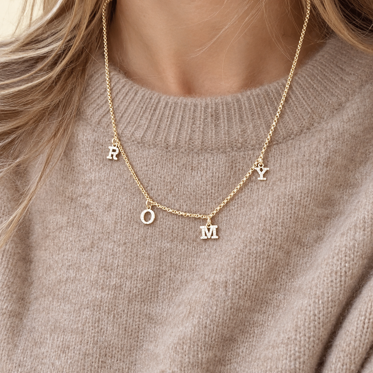 Personalisierte GINA Goldkette mit vier Buchstabenanhängern, getragen an einer frau. Eine zarte Kette mit den Initialen der Kinder als liebevolles Geschenk zur Geburt für die frischgebackene Mama, vom Papa oder Partner mit anfangsbuchstaben der familie in 333 Gold, 585 Gold und 750 Gold. 