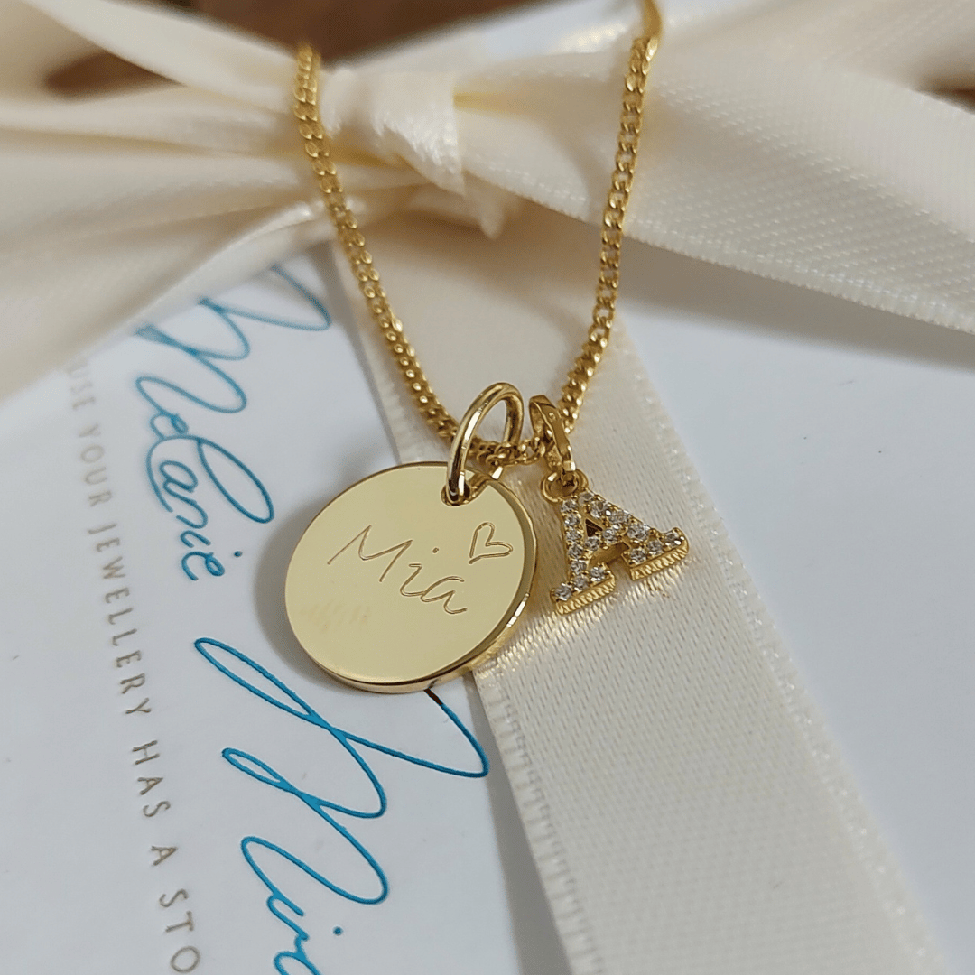 Die EDITH Goldkette vereint einen funkelnden Buchstaben-Anhänger mit einem Gravur-Plättchen – ein Geschenk zur Geburt mit dem Namen des Babys graviert.
