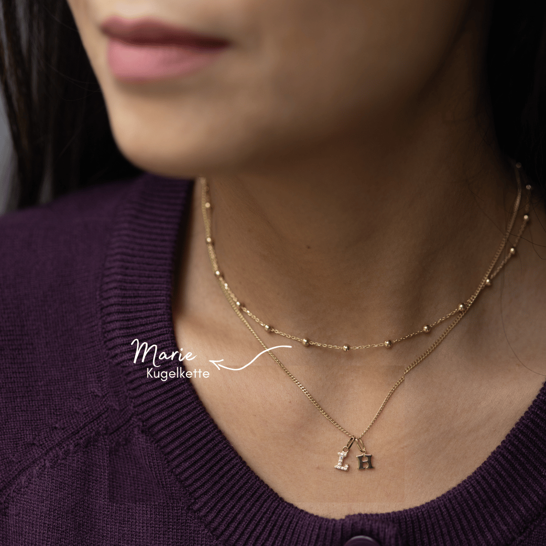 Unsere edle CAMILA Kette mit zwei edlen Buchstaben-Anhängern aus Echtgold, elegant am Hals getragen. Die Buchstaben Kette mit Euren beiden Initialen ist ein Zeichen der Verbundenheit als Geschenk zu Eurem Hochzeitstag. Handgefertigt in 333 Gold in unserer Berliner Goldschmiede