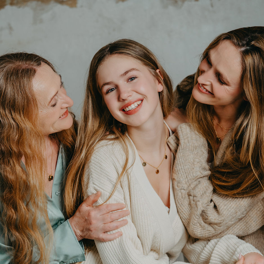Mädchen mit Mama und Oma an der Seite trägt ihre erste eigene goldkete mit drei kleinen Gravuranhängern, die individuell mit Namen, Initialen oder einer liebevollen Botschaft personalisiert werden können. Der filigrane Schmuck für Mädchen ist ein besonderes Geschenk von Mama oder Papa zum Geburtstag, zur Einschulung oder zum Schulabschluss. Die Kette symbolisiert Geborgenheit, Familienliebe und die besondere Verbindung zwischen Eltern und Tochter.