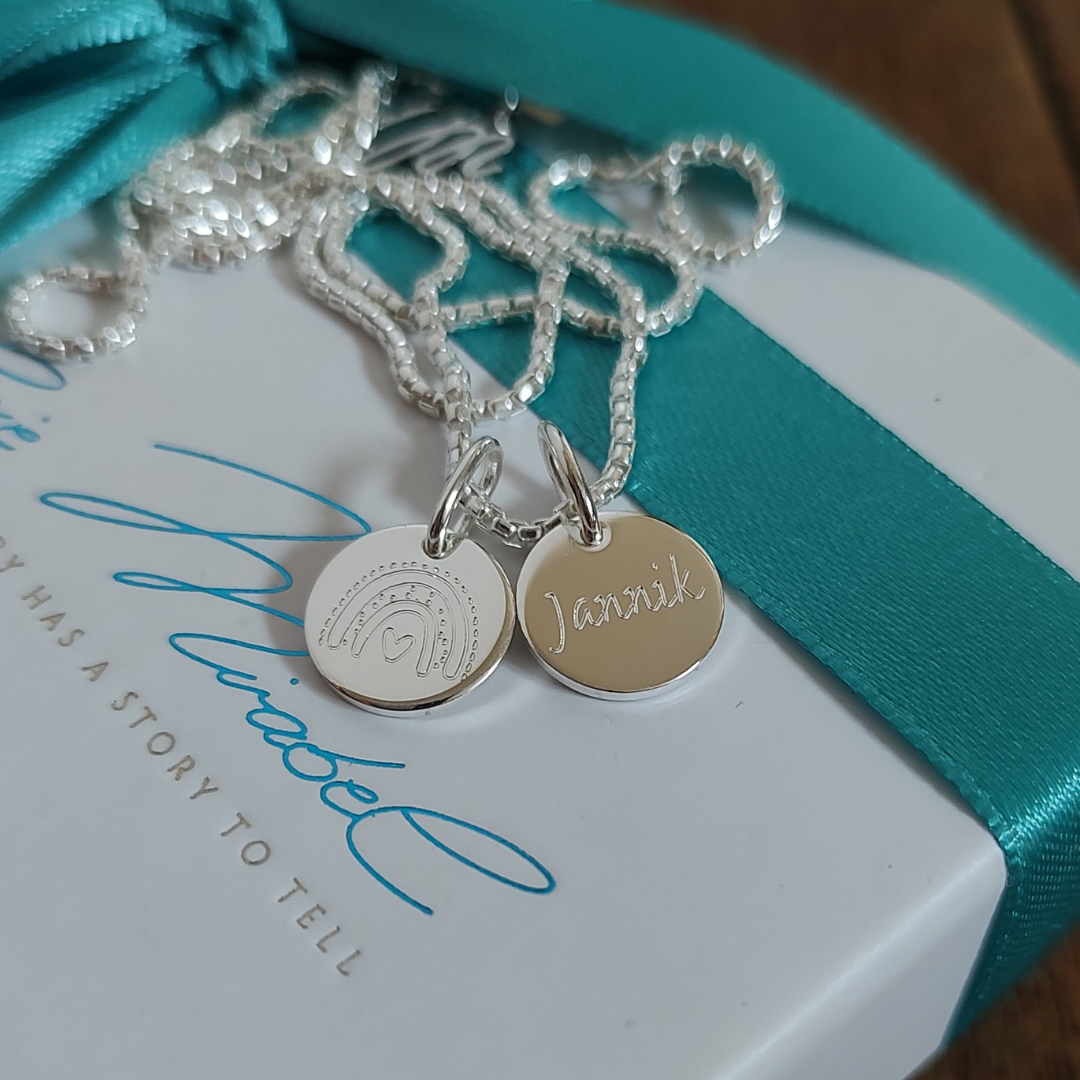 Detailsansicht auf die Gravuren unser meistverkauften Initialenkette - ein perfektes geschenk vom Ehemann an seine Ehefrau zur Geburt ihrer Kinder, um die Liebe und Verbundenheit auszudrücken. Wir personalisieren die Plättchen mit Kindernamen, Baby Fussabdrücken, Geburtsblumen und vieles mehr in unserem Berliner Atelier